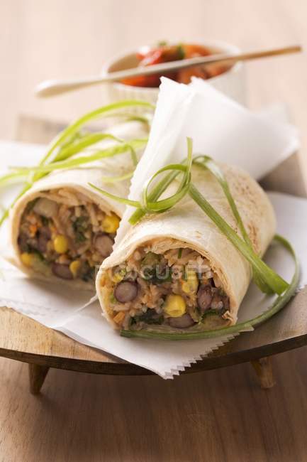 Bean burritos wrapped in paper on wooden stand over table — Stock Photo