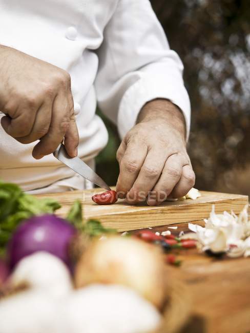 Closeup view of a chef slicing a chilli pepper on wooden desk — Stock Photo