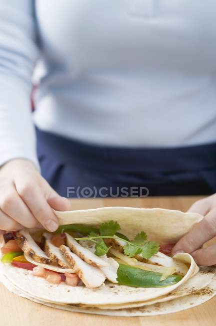 Vista de cerca de la persona plegable Tortilla sobre relleno de pollo - foto de stock