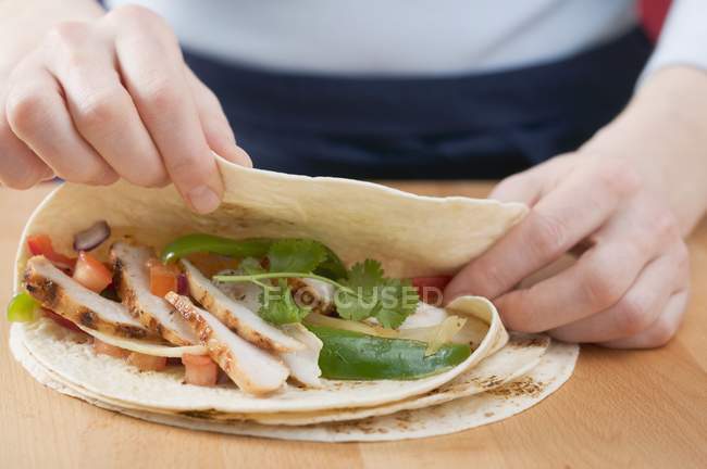 Abgeschnittene Nahaufnahme von Händen, die Tortilla über Hühner- und Gemüsefüllung falten — Stockfoto