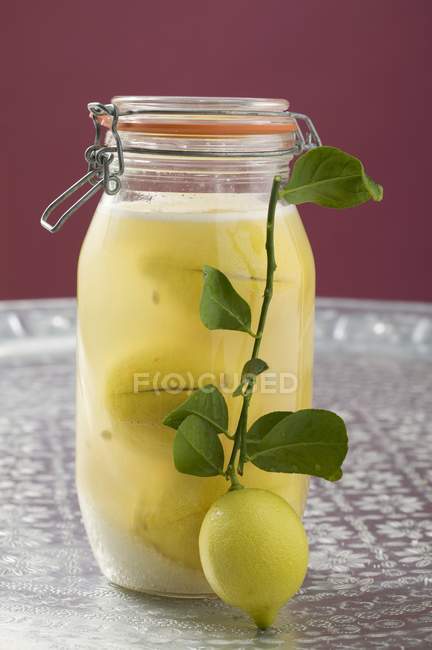 Vista de cerca de limones en escabeche en frasco con rama pequeña y limón fresco - foto de stock