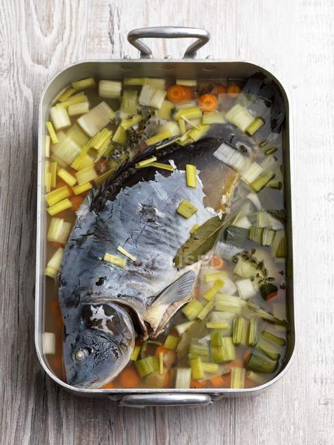 Vue du dessus de la carpe pochée avec des légumes dans un plat de cuisson sur une surface en bois — Photo de stock