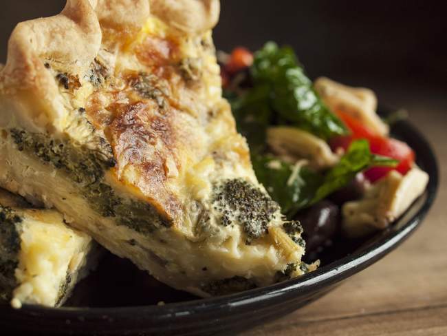 Piece of Broccoli Quiche with a Side Salad on black plate over wooden surface — Stock Photo