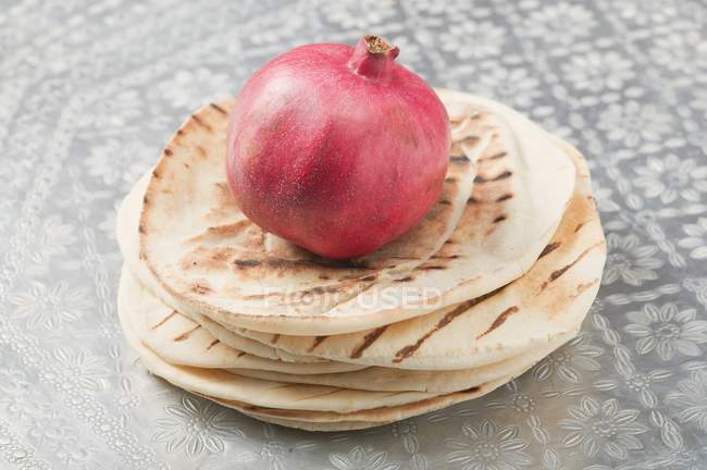 Pomegranate on a stack of flatbread over tablecloth — Stock Photo