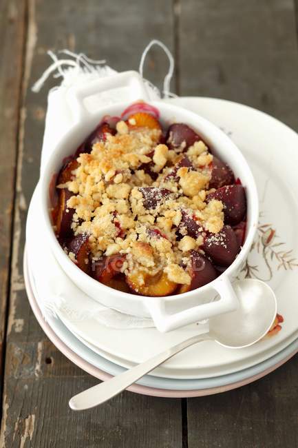 Plum Crumble in Individual Baking Dish and Spoon over stacked plates — Stock Photo
