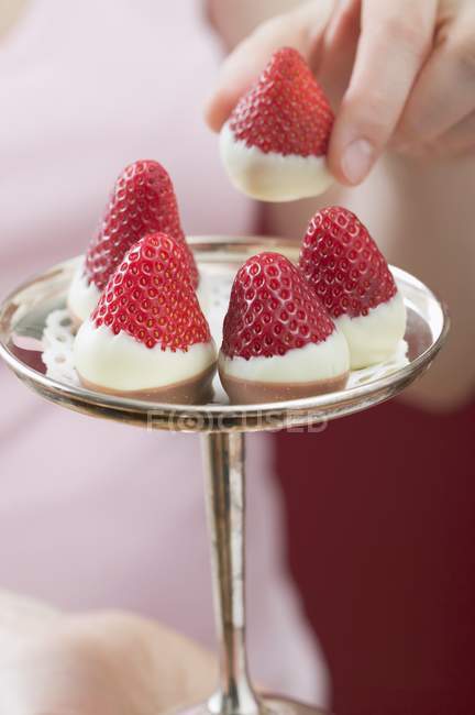 Closeup cropped view of hand taking chocolate-dipped strawberry from silver stand — Stock Photo