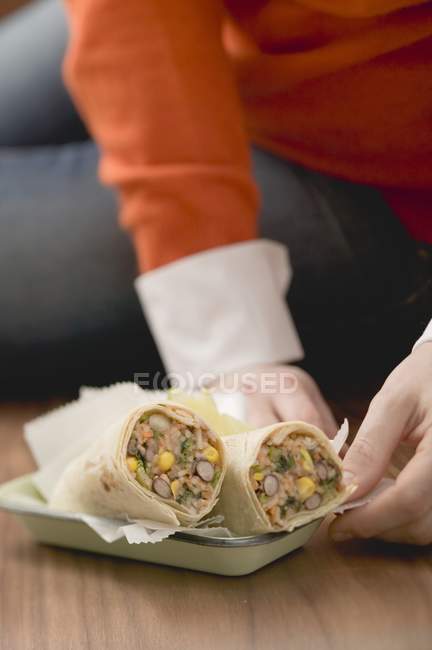 Nahaufnahme einer Person, die mit Burritos auf dem Teller auf dem Boden sitzt — Stockfoto