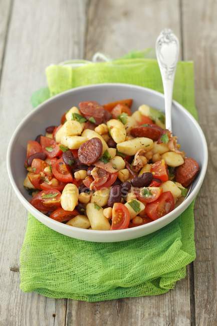 Gnocchi with chorizo, kidney beans and cherry tomatoes  on white plate over green towel — Stock Photo