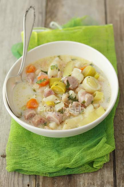 Soup with veal sausage, leek and gnocchi on white plate  over green towel  on wooden surface — Stock Photo