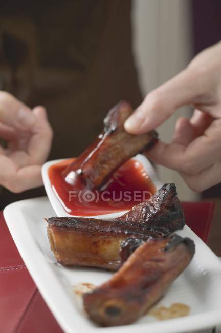 Frau taucht glasierte Schweinerippe — Stockfoto
