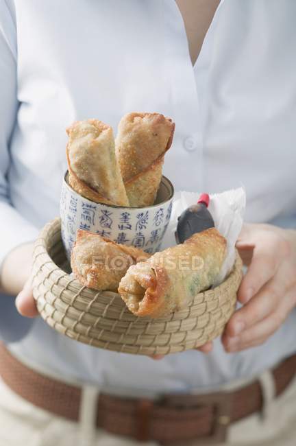 Cropped view of woman holding basket of spring rolls and soy sauce — Stock Photo