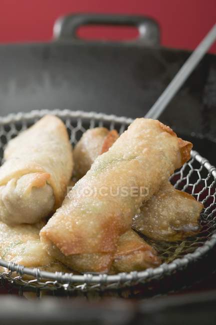 Closeup view of deep-fried spring rolls in a skimmer and wok — Stock Photo