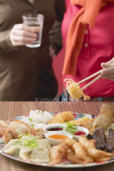 Vista recortada de dos mujeres con plato de aperitivos asiáticos - foto de stock