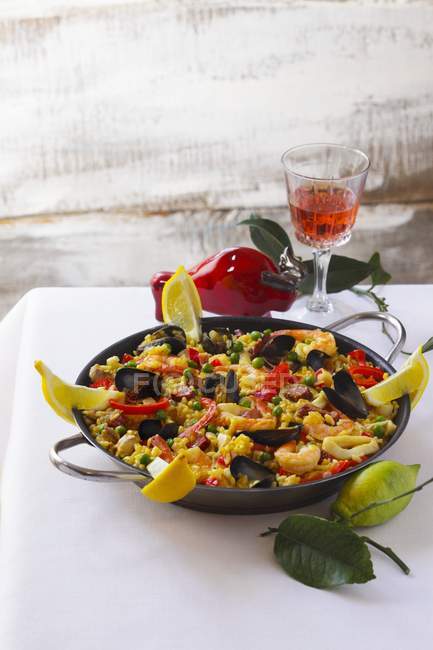 A pan of mixed paella and a glass of wine on pan over tablecloth — Stock Photo