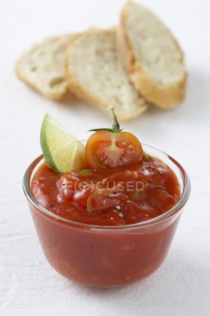 Sumerja de tomate con cuña de lima, rebanadas de pan blanco en la superficie blanca - foto de stock