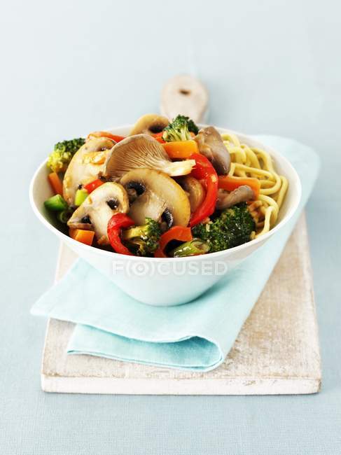 Remover las setas fritas y las verduras con fideos en un tazón azul sobre una toalla - foto de stock