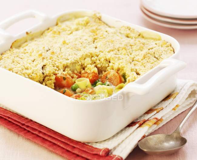 Vegetable bake with crumbles in white dish over towel on table with spoon — Stock Photo