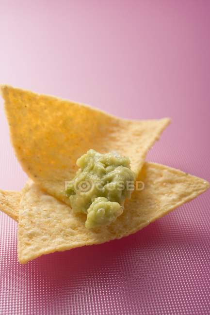 Гуакамоле на чипсах с тортильей на розовой поверхности — стоковое фото