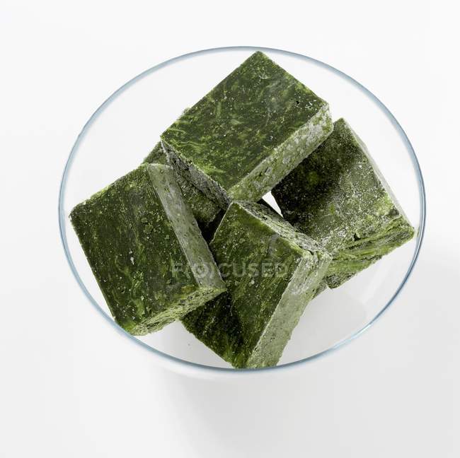 Cubes of frozen spinach in a glass bowl  on white surface — Stock Photo