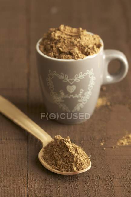 Carob gum in mug over wooden surface — Stock Photo