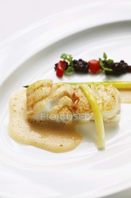 Closeup view of fried cod with lentils, tomato broth and leek — Stock Photo