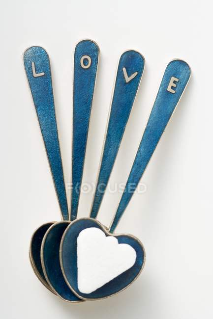 Closeup view of heart-shaped spoons with sugar lump and the word Love — Stock Photo