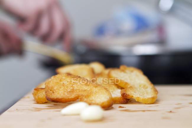 Toasted baguette slices being rubbed with garlic on wooden surface — Stock Photo