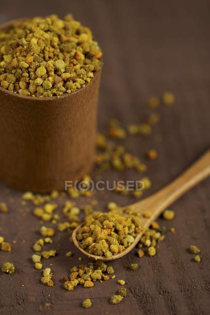 Gránulos de polen de abeja en una taza de madera, en una cuchara y alrededor - foto de stock