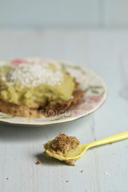 Тарталетка со сладким гороховым кремом и кокосом на белой тарелке над деревянной поверхностью с ложкой — стоковое фото