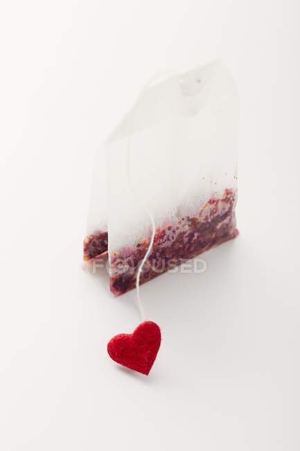 Vue rapprochée d'un sachet de thé avec coeur rouge sur surface blanche — Photo de stock
