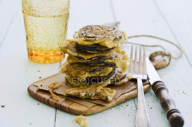 Deep-fried slices of aubergine on wooden desk with fork and knife — Stock Photo