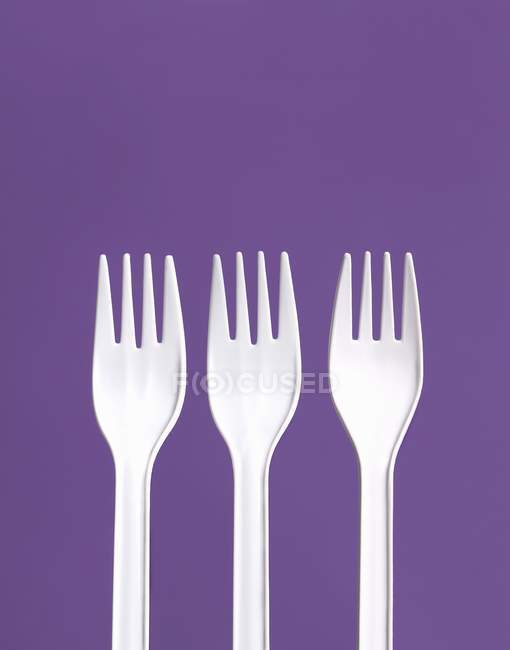Vista de cerca de tres tenedores de plástico blanco sobre un fondo púrpura - foto de stock