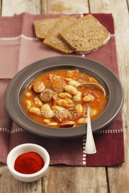 Fasolka po bretonsku - beans with sausage and bacon in tomato sauce  on black plate over towel — Stock Photo