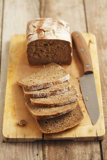 Elevated view of a sliced wholemeal bread loaf with a knife on a chopping board — Stock Photo