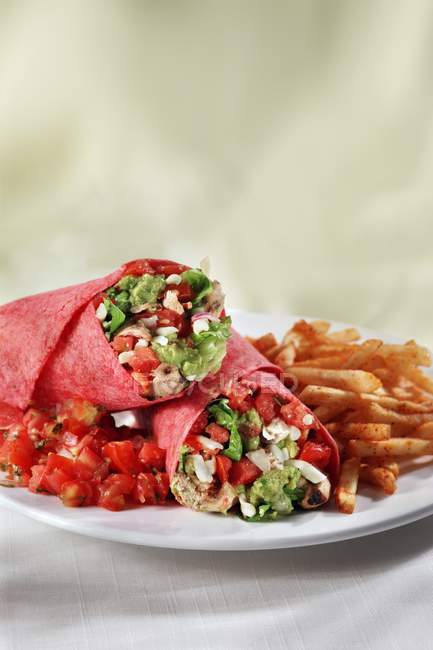 Курица и овощная обертка с гуакамоле; сальса и картофель фри на белой тарелке — стоковое фото
