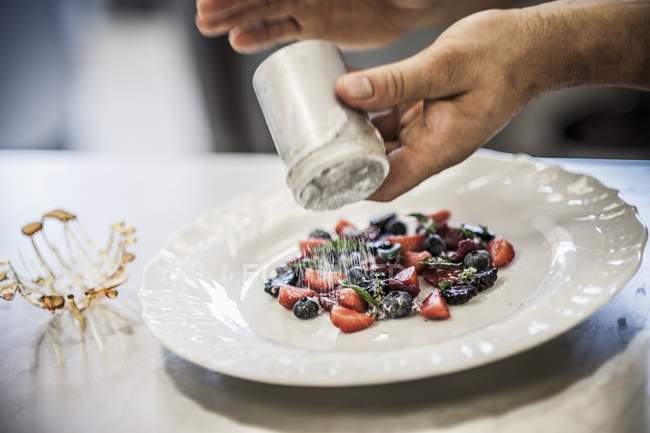 Closeup cropped view of person sprinkling berries with sugar — Stock Photo