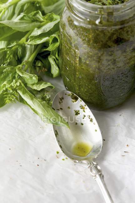 Primo piano vista del Pesto fatto in casa in un barattolo con cucchiaio sporco e basilico fresco — Foto stock