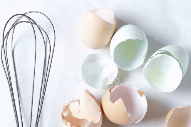 Vista dall'alto di gusci d'uovo pastello incrinati e una frusta — Foto stock