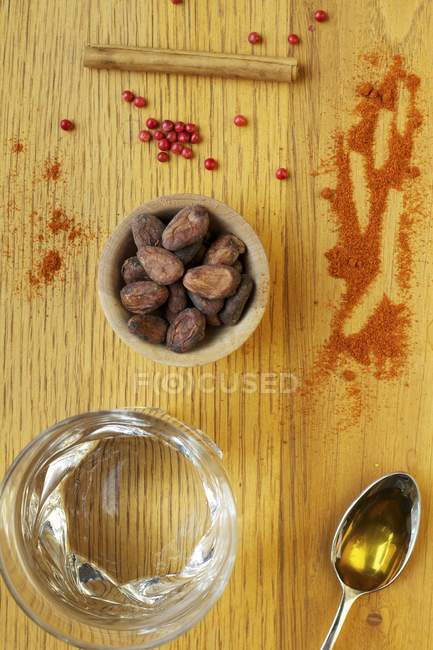 Top view of cocoa beans with red berries, oil, water, cinnamon stick and powdered spice — Stock Photo
