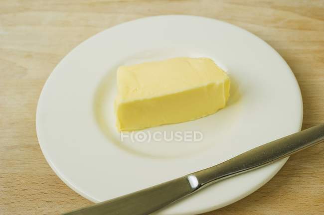 Closeup view of a pat of butter on a plate with a knife — Stock Photo