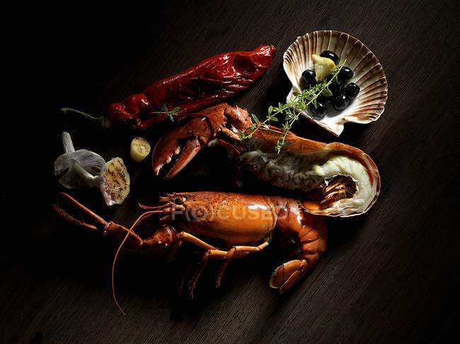 A still life including lobster, olives and thyme on dark surface — Stock Photo