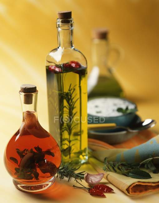 Flavoured oil and vinegar in bottles; a bowl of herb sauce in the background — Stock Photo