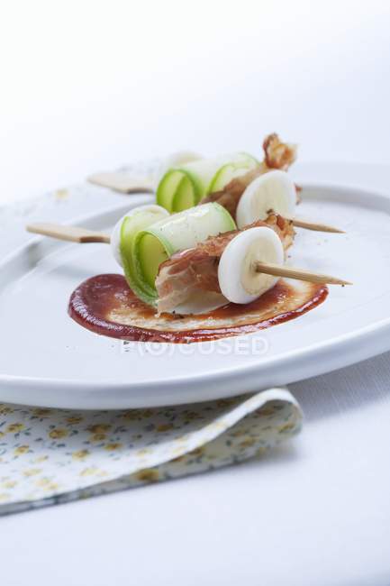 Skewers of egg, courgette and bacon  on white plate — Stock Photo