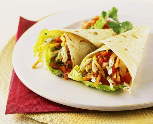 Chicken and vegetable wraps on white plate over red towel — Stock Photo
