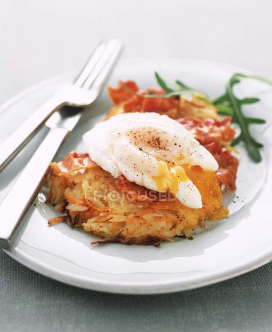 Batata e cenoura fritter coberto com um ovo escalfado em placa branca com garfo e faca — Fotografia de Stock