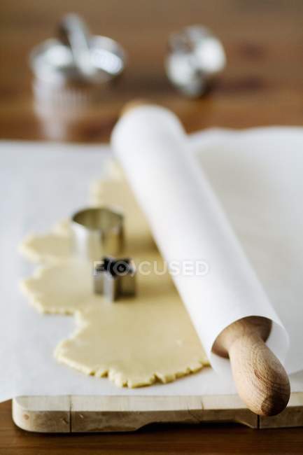 Повышенный вид развернутого теста для печенья со скалкой в бумаге и кусачками для печенья — стоковое фото