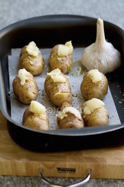 Pommes de terre crues Hasselback dans une boîte de rôtissage, assaisonnées de sel, poivre et beurre d'ail — Photo de stock