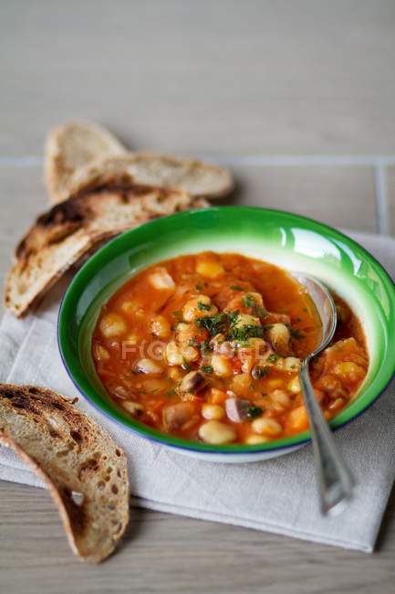 Bean and chickpea stew with toasted bread on green plate with spoon — Stock Photo