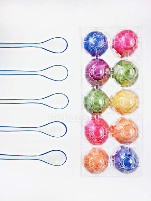 Top view of ten eggs, colored for Easter, in a transparent egg box with egg spoons — Stock Photo