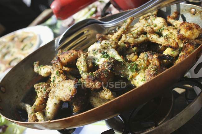 Closeup view of breaded frog legs with herbs and cutlery — Stock Photo